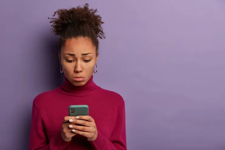 people unhappy emotions concept sad disappointed woman received bad sms holds smartphone concentrated screen with dissatisfaction wears burgundy poloneck poses indoor feels lonely
